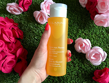 Bain Tonic aux plantes de Clarins sur un fond vert avec des fleurs.