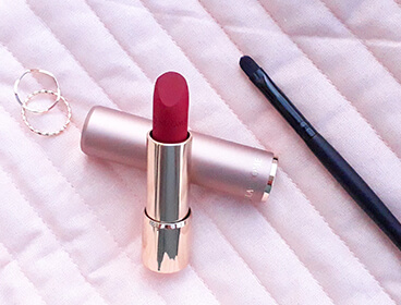 Rouge à lèvres Lancôme ouvert avec un pinceau à lèvres sur un fond rose.