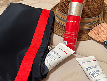 Coffret Men Energisant de Clarins composé d'une trousse de voyage, d'un shampoing douche, d'un nettoyant visage et d'un gel énergisant sur un fond beige