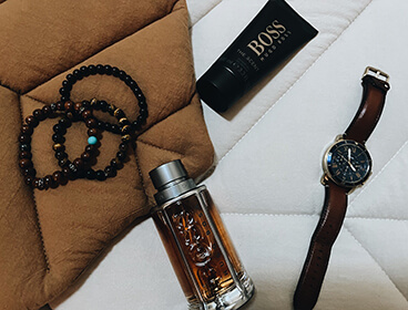 Deux produits Hugo Boss, le parfum Boss The Scent et le gel douche sur un fond beige et avec une montre.