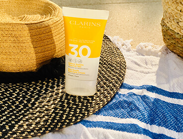 Crème solaire visage Clarins SPF 30 avec un chapeau et une serviette de plage