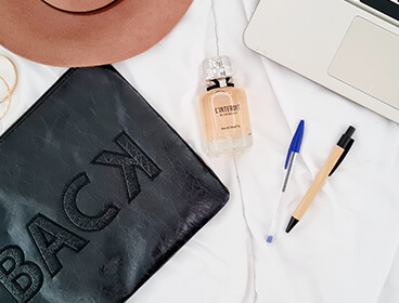 Parfum L'Interdit de Givenchy sur un fond blanc avec un ordinateur et des stylos.